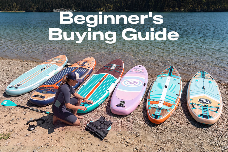 A person kneeling beside six paddle boards on a lakeshore, with the text “Beginner’s Buying Guide.”